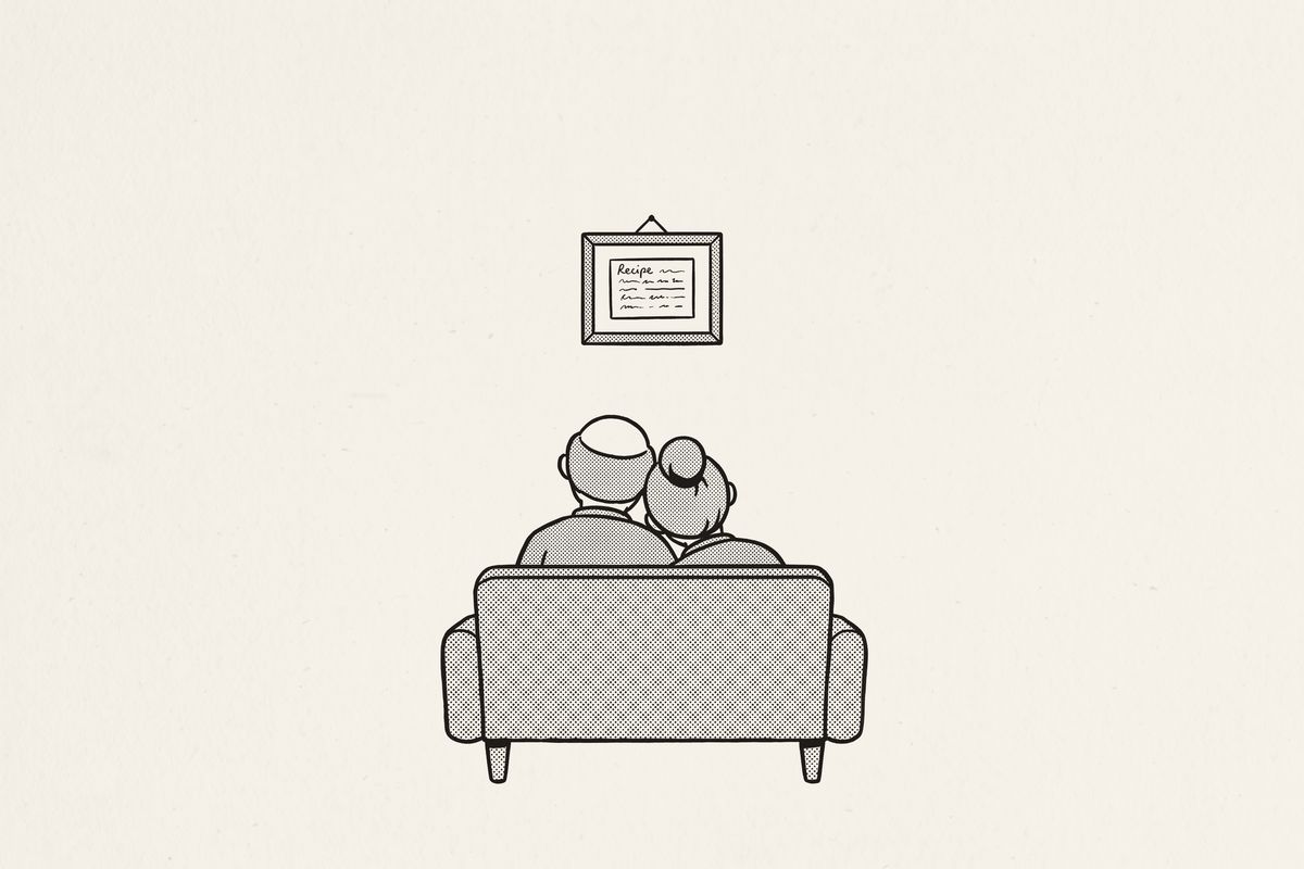 An older couple on a sofa, her head on his shoulder, looking up at a framed recipe card.