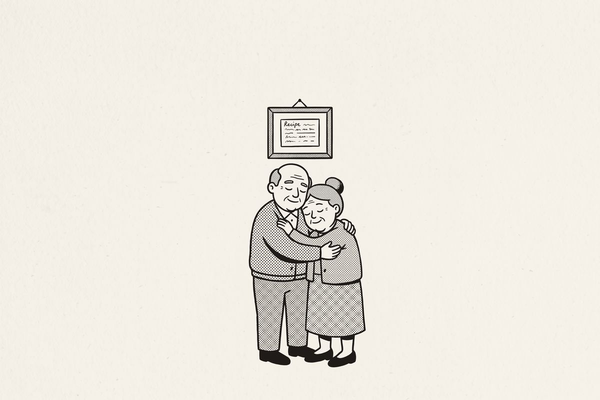 An older couple slow-dancing in their kitchen beneath a framed recipe card.