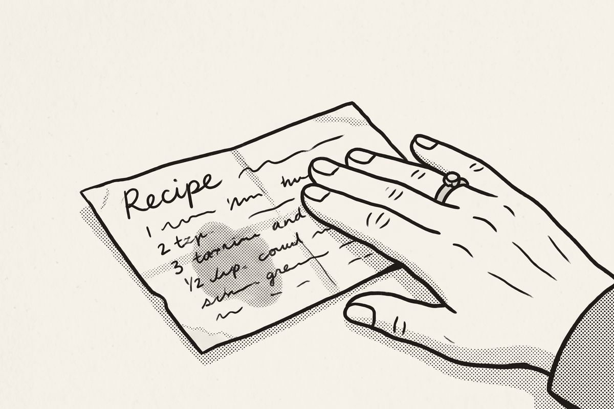 An elderly hand resting on a stained, folded handwritten recipe card.