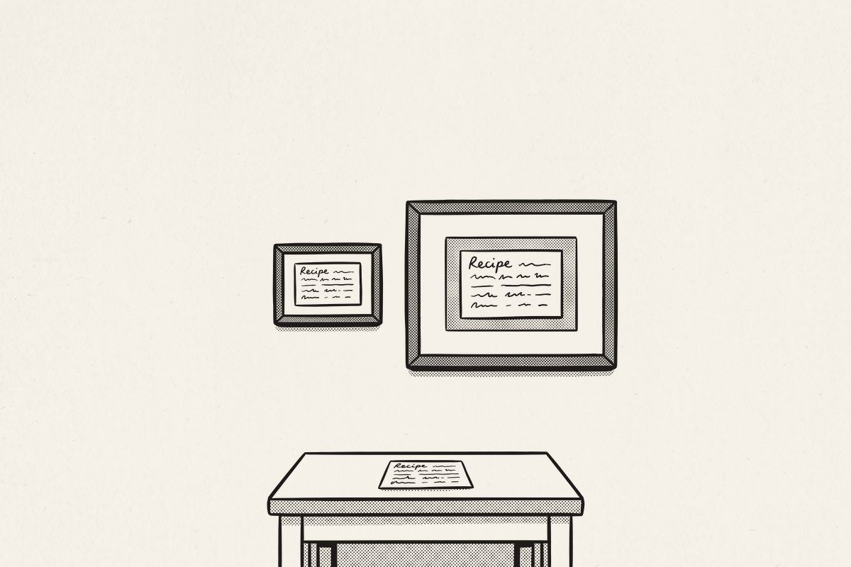 A small framed recipe card and a larger framed print of a card on a wall, the original card on the table below.