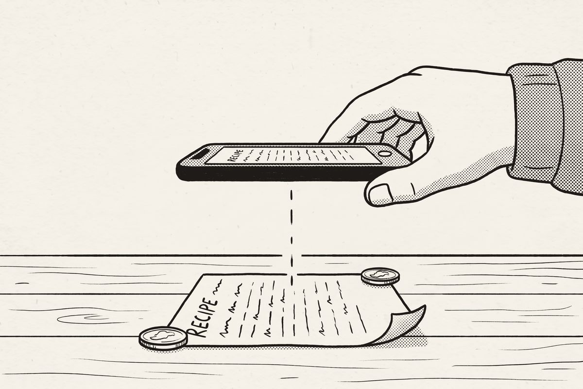 A phone held flat directly above a recipe card, two coins holding down its corners.
