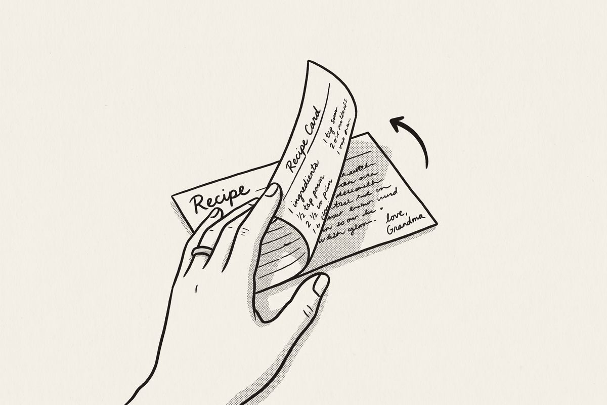 A hand turning a recipe card over to show more writing on its back.