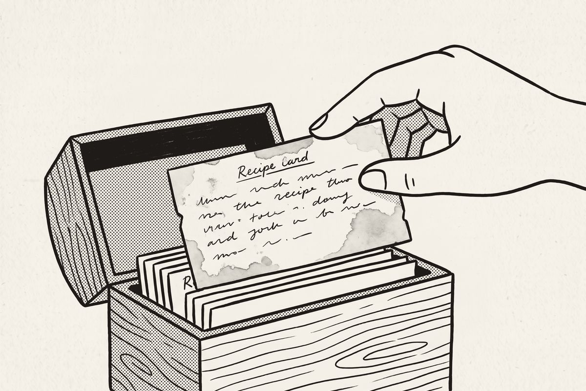 A hand tucking a worn recipe card back into the recipe box.