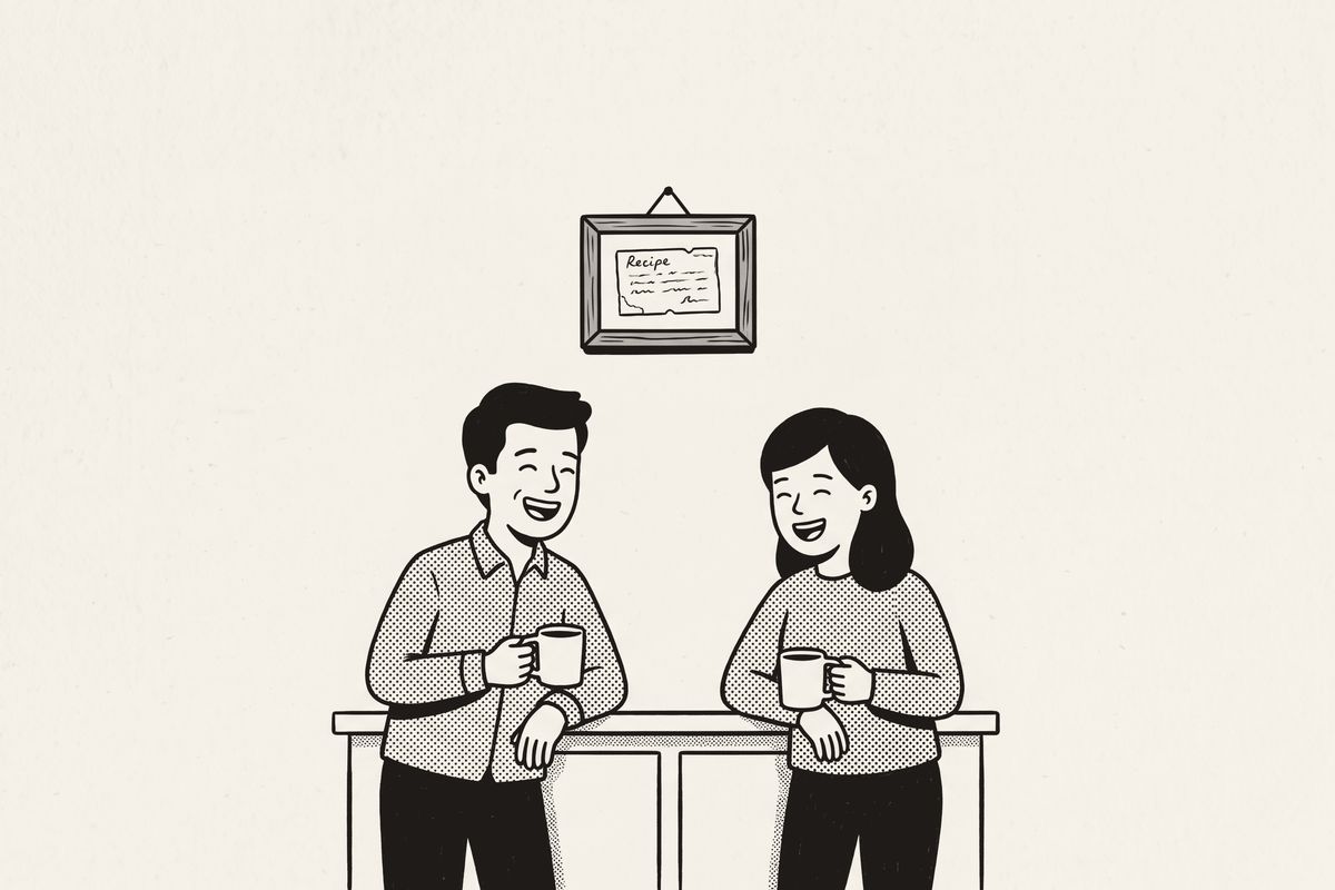 A brother and sister laughing in the kitchen beneath a framed family recipe card.