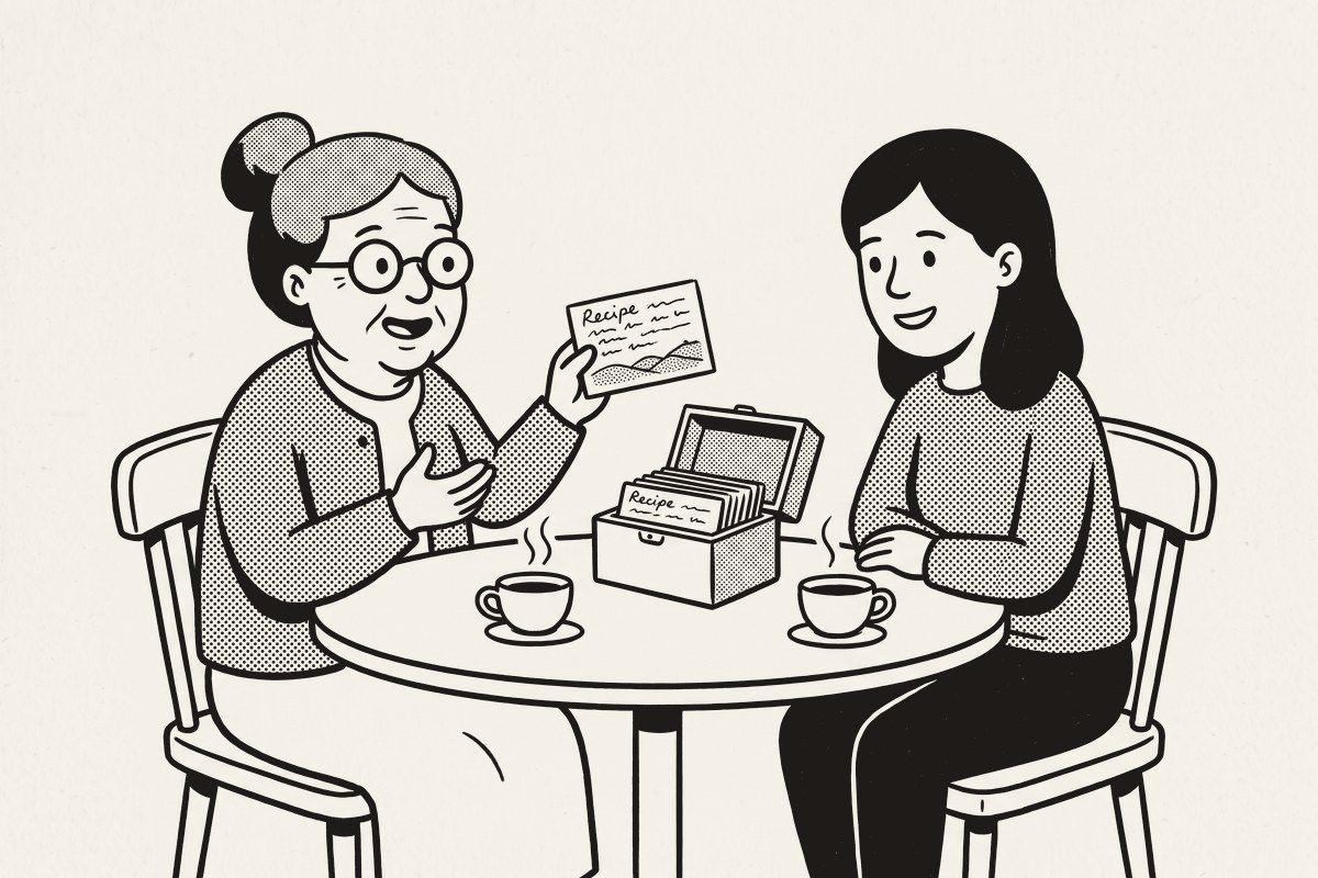 Two women at a kitchen table, one holding up a recipe card, the open recipe box between them.