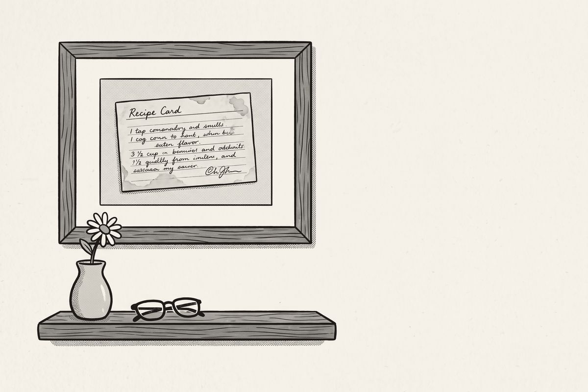A framed recipe card on a kitchen wall, above a shelf with a single flower and reading glasses.