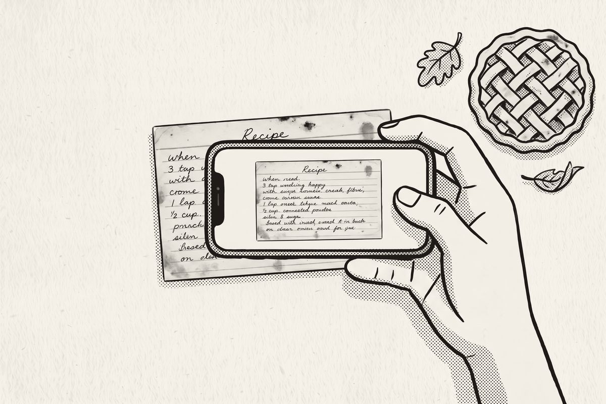A hand holding a phone over a handwritten recipe card, beside a lattice pie and autumn leaves.
