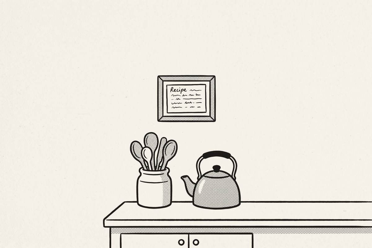 A framed recipe card on a kitchen wall, above a jar of wooden spoons and a kettle.