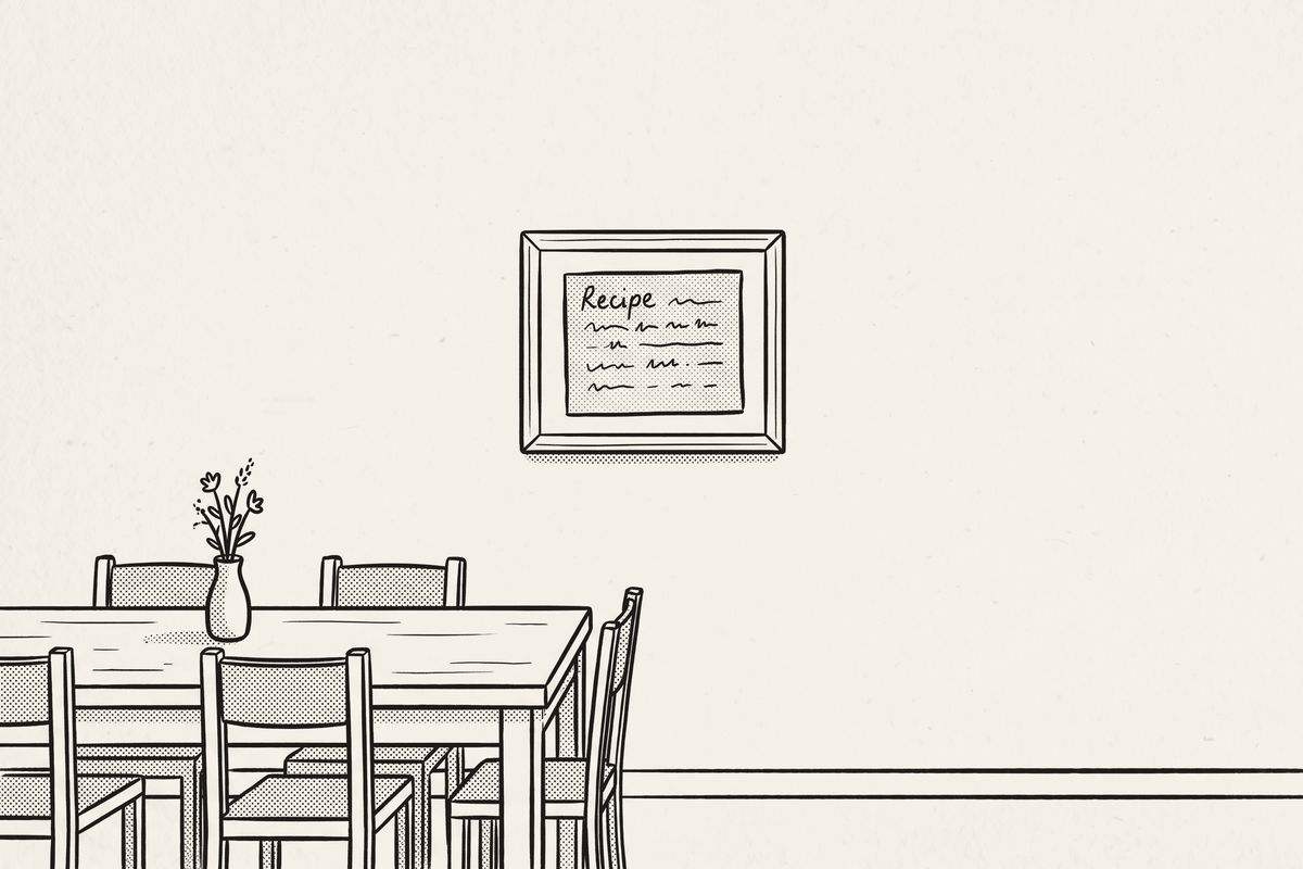A dining table with chairs and a framed recipe card on the wall across from it.