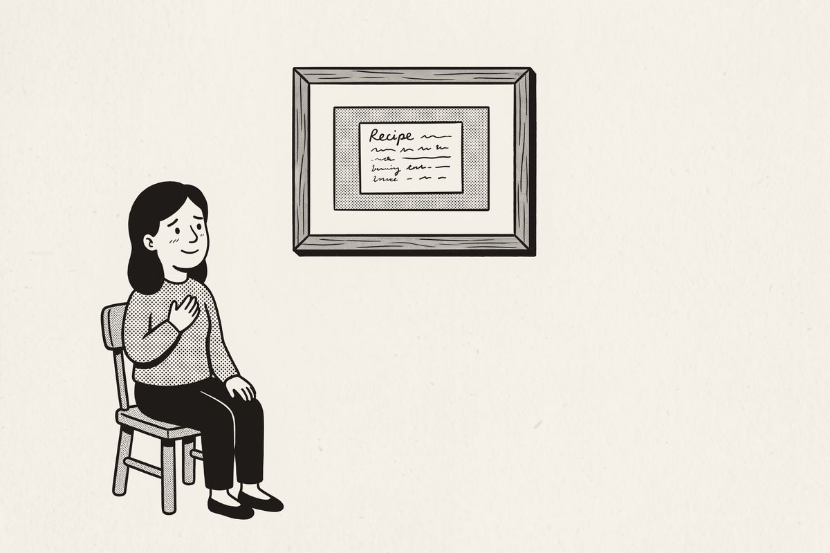 A woman on a chair, hand on her heart, looking up at her mother's framed recipe card.
