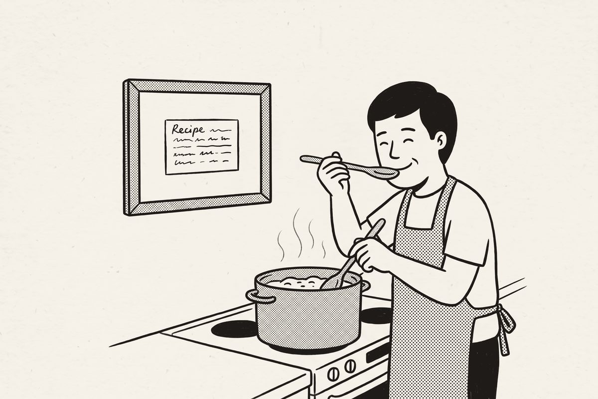A dad in an apron tasting from the pot, a framed recipe card on the wall above the stove.