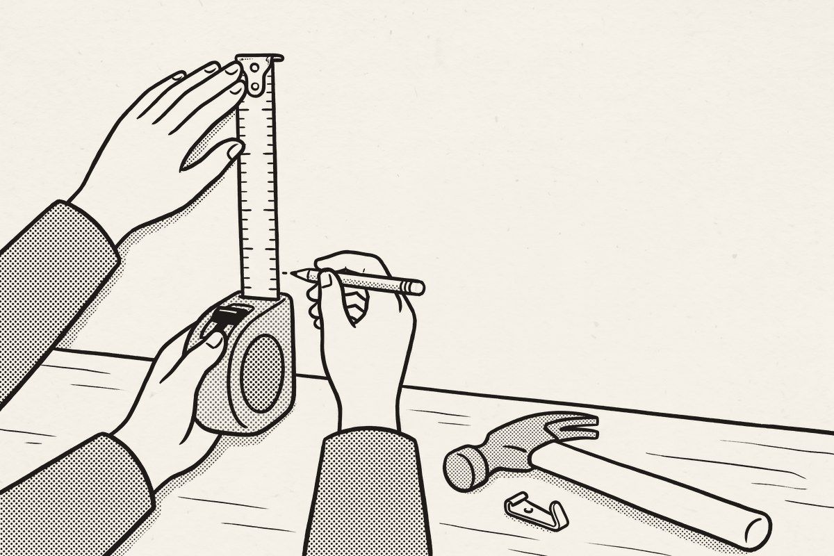 A hand holding a tape measure against a kitchen wall and making a pencil mark.