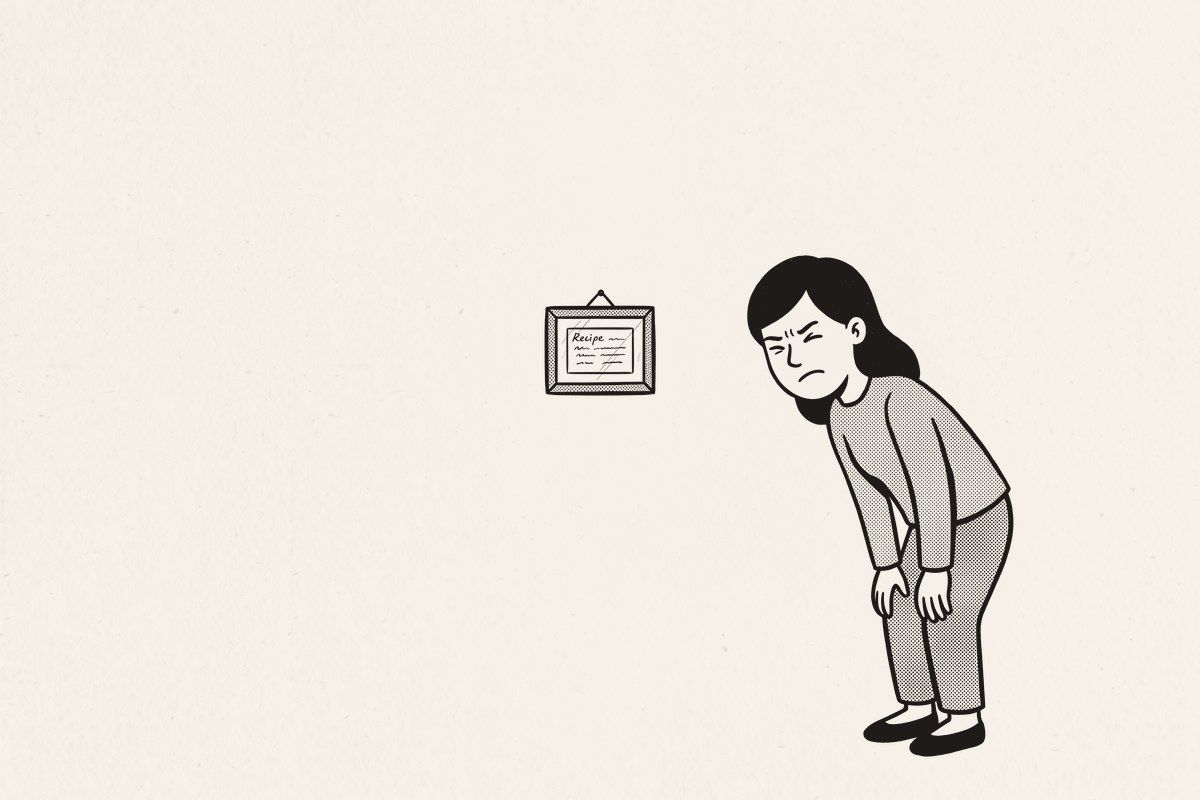 A woman squinting at a tiny framed recipe card in the middle of a big kitchen wall.