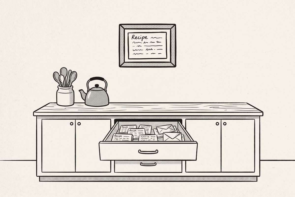 A kitchen drawer of old recipe cards pulled open, with one framed card on the wall above the counter.