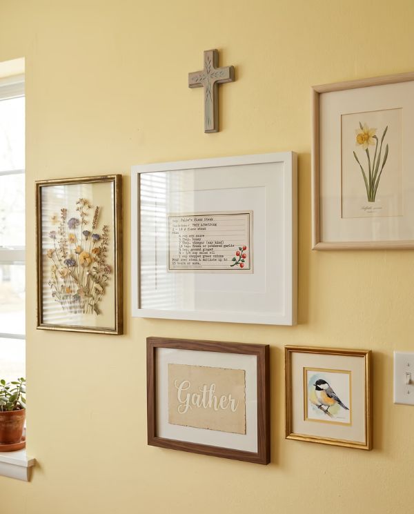 Framed recipe cards among family pictures on a yellow wall.